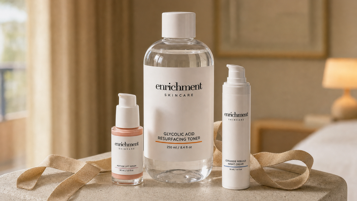 Three Enrichment Skincare bottles, including Glycolic Acid Resurfacing Toner, with a loose linen ribbon on a stone surface