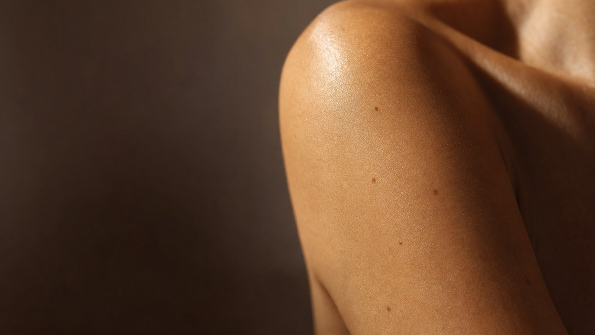 Close-up of a bare shoulder with a few small freckles and sun spots in warm light