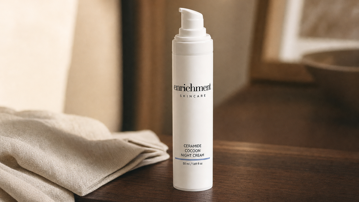 Enrichment Skincare Ceramide Cocoon Night Cream pump bottle on a wooden bedside table beside a folded linen cloth