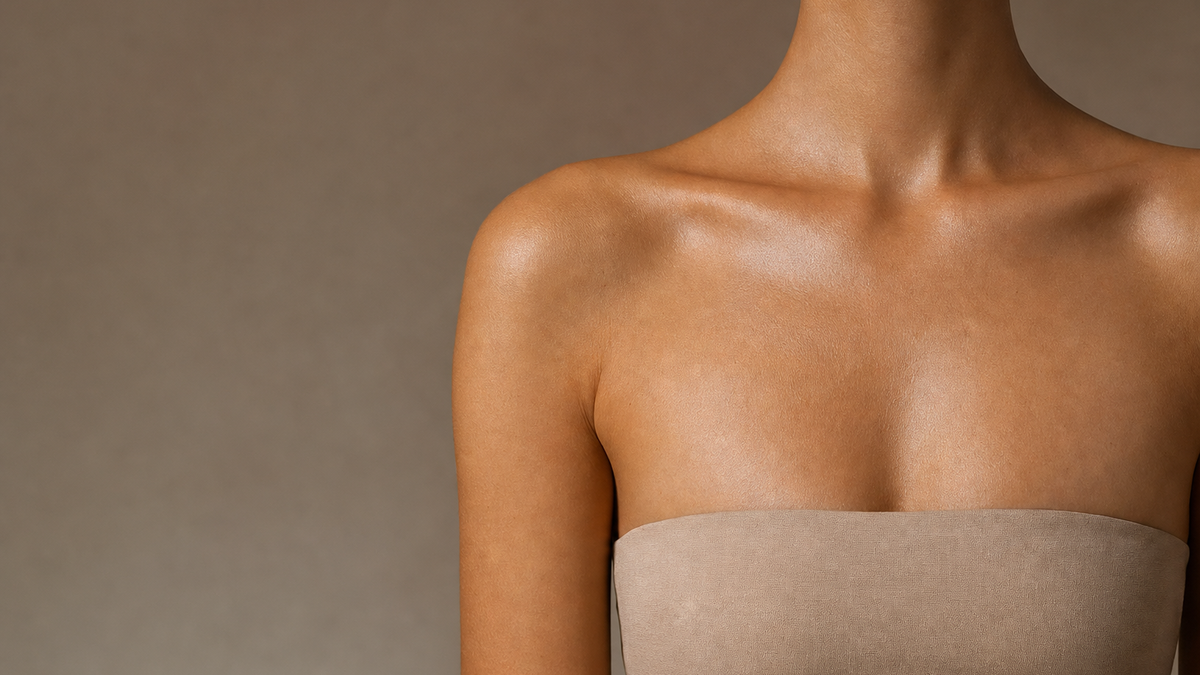 Close-up of a woman's bare shoulders, collarbones and neck against a warm neutral background