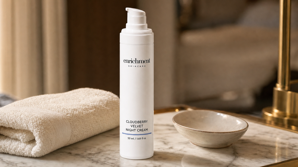 Enrichment Skincare Cloudberry Velvet Night Cream on a marble vanity beside a folded towel and a small ceramic dish