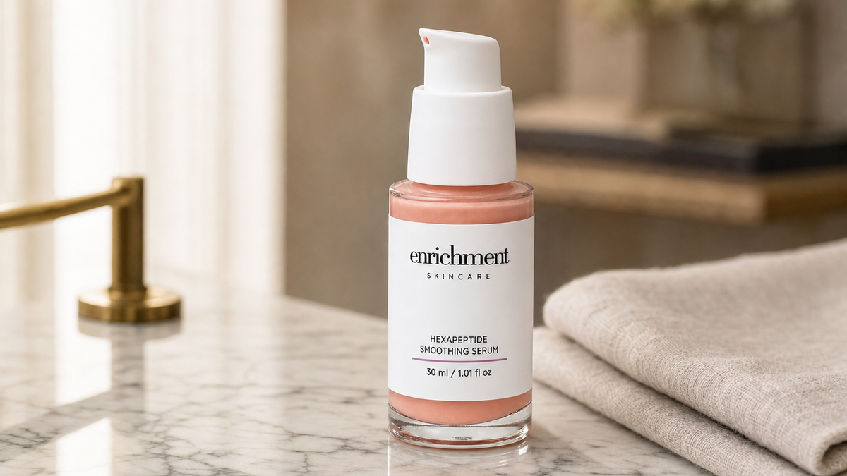 Enrichment Skincare Hexapeptide Smoothing Serum on a marble vanity beside folded linen and a brass tap
