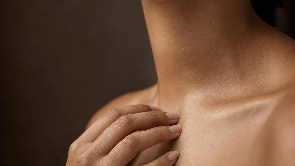 A gentle hand at the collarbone, structure caught in light
