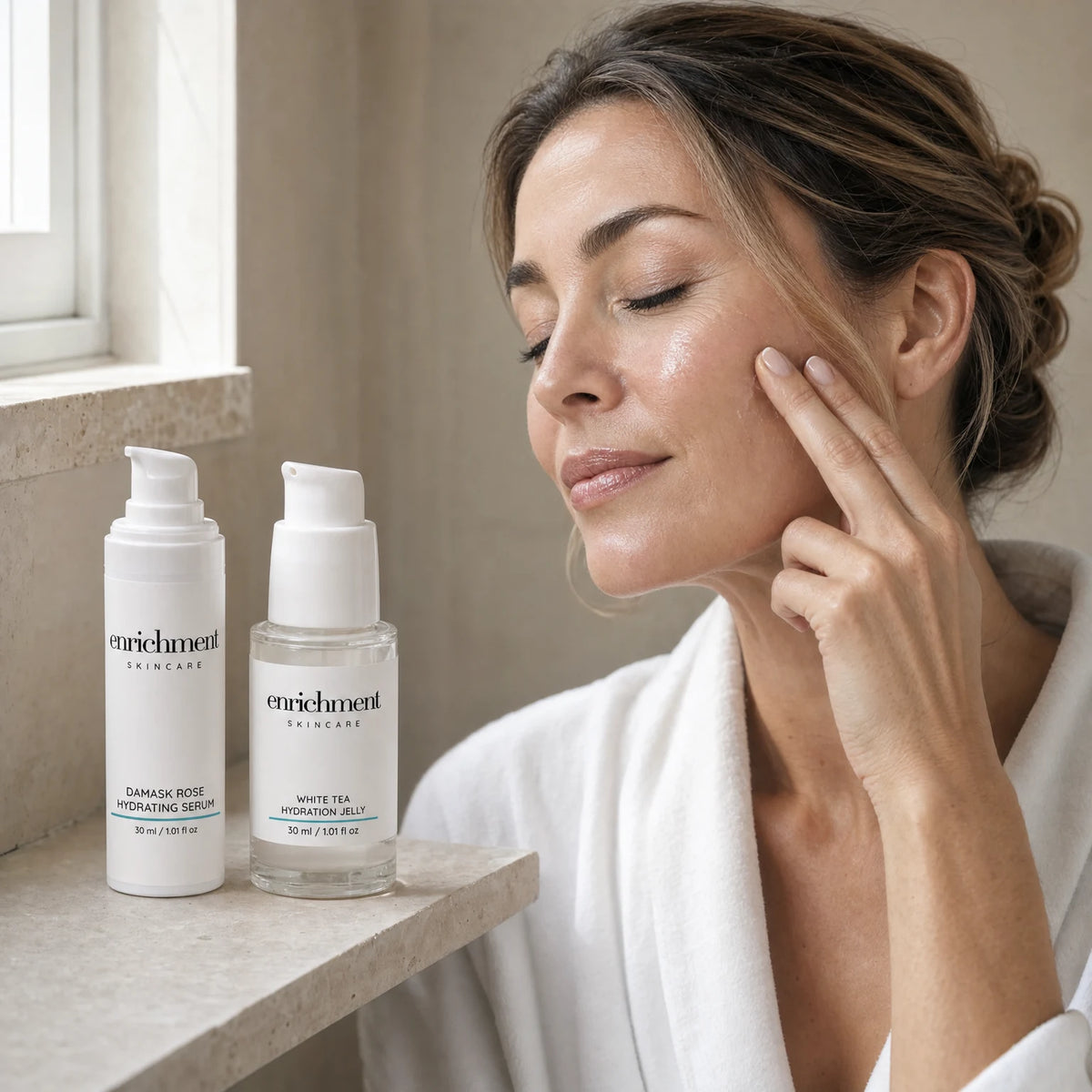 A woman in her forties pressing serum into her cheek beside a stone window shelf, with the two products of the Duo in front of her