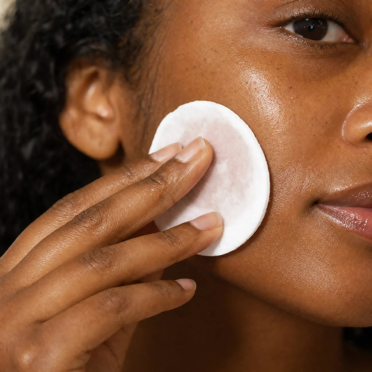 Hand applying Damask Rose Hydrating Toner with a cotton pad to the cheek