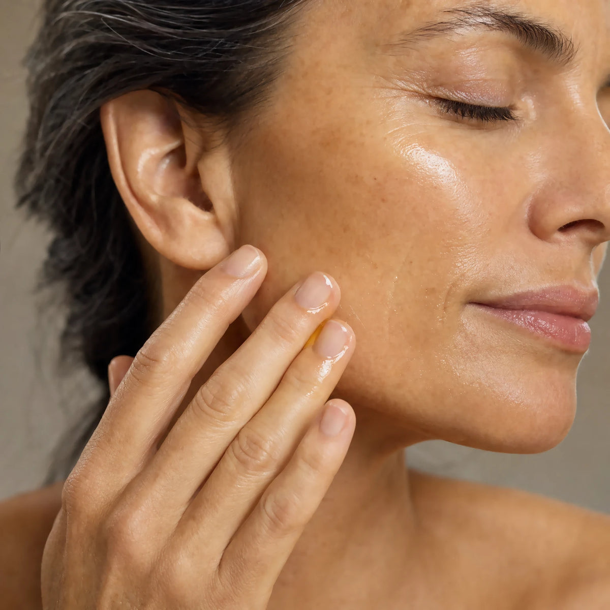 Woman in her mid-forties applying Enrichment Bakuchiol Refining Oil Serum to her cheek