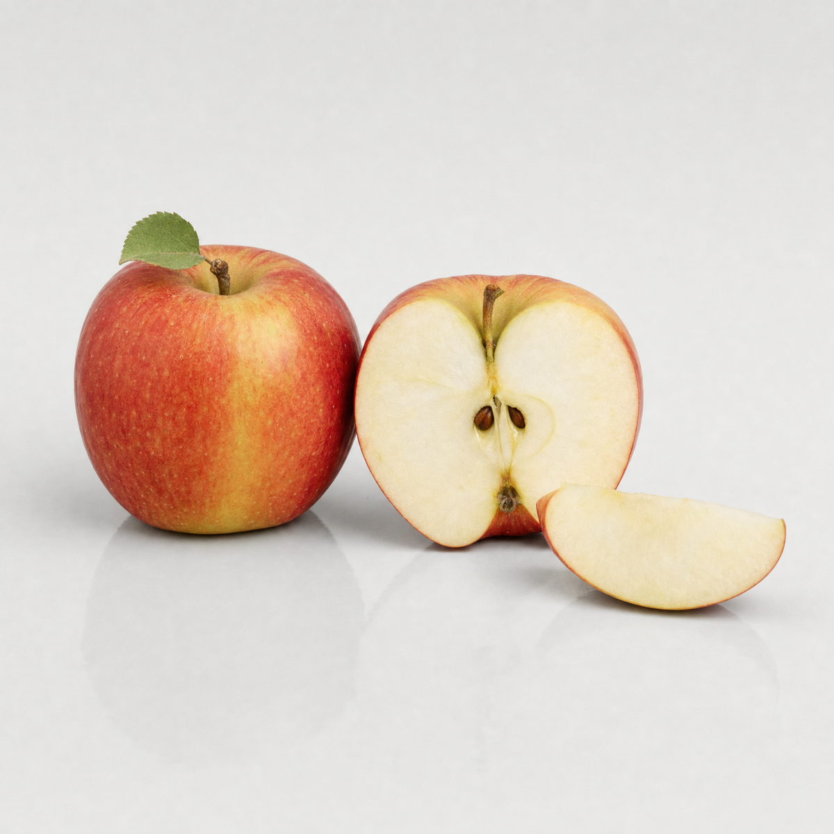 A whole red-blushed apple beside an apple cut in half to show its core and pips
