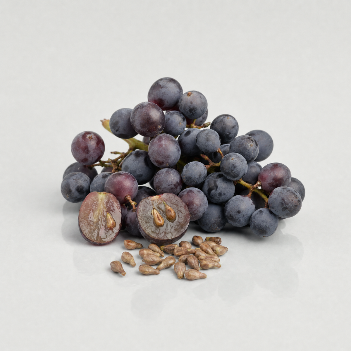 A bunch of dark red grapes, two halved to show their seeds, beside a small heap of grape pips