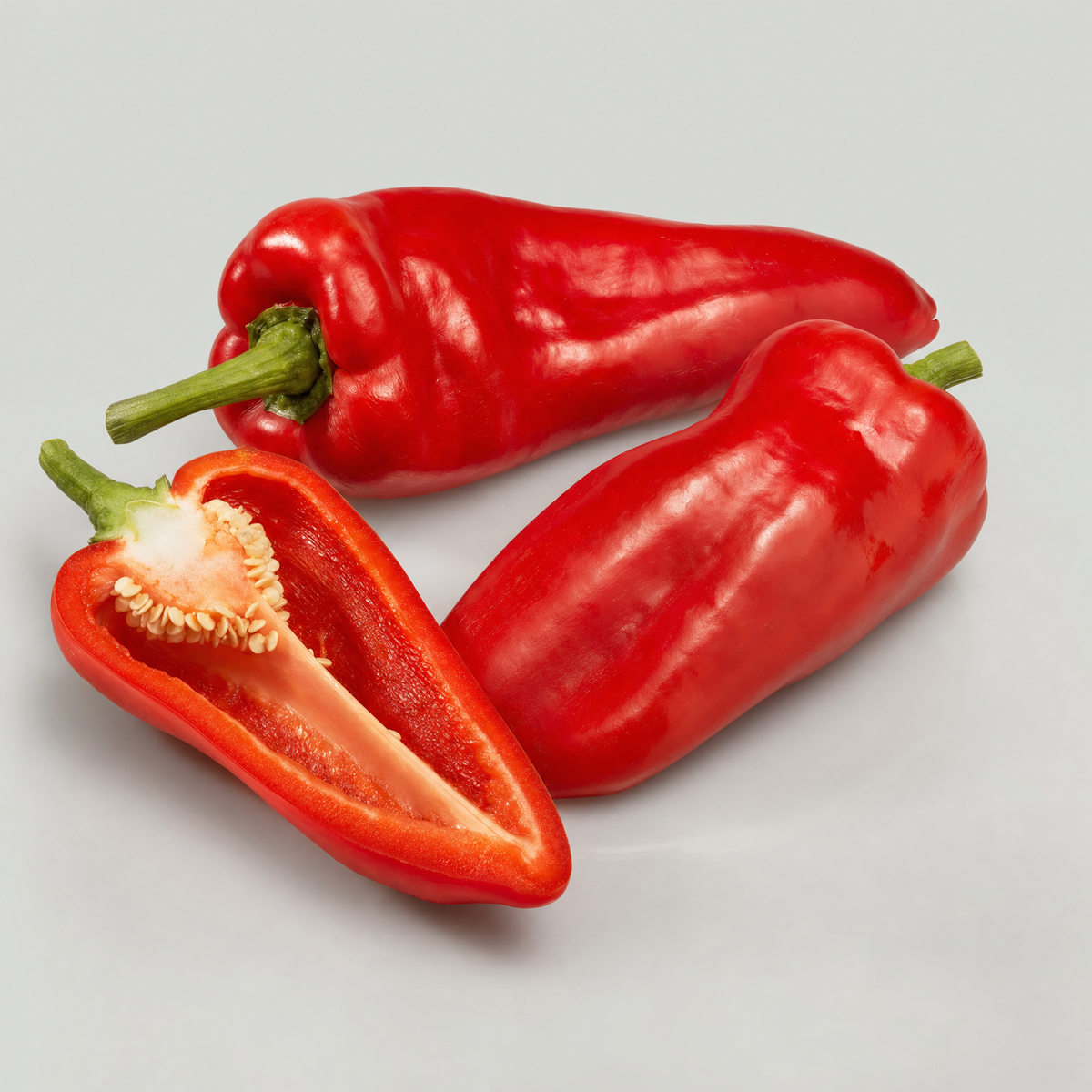 Two sweet red paprika peppers, one cut open to show its seeds