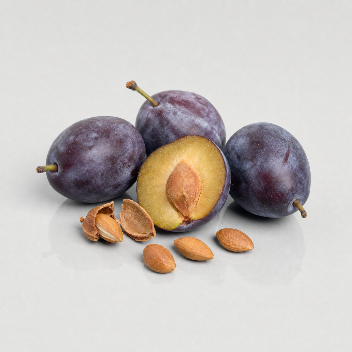 Ripe purple plums, one halved with its stone, beside cracked stones and almond-shaped plum kernels