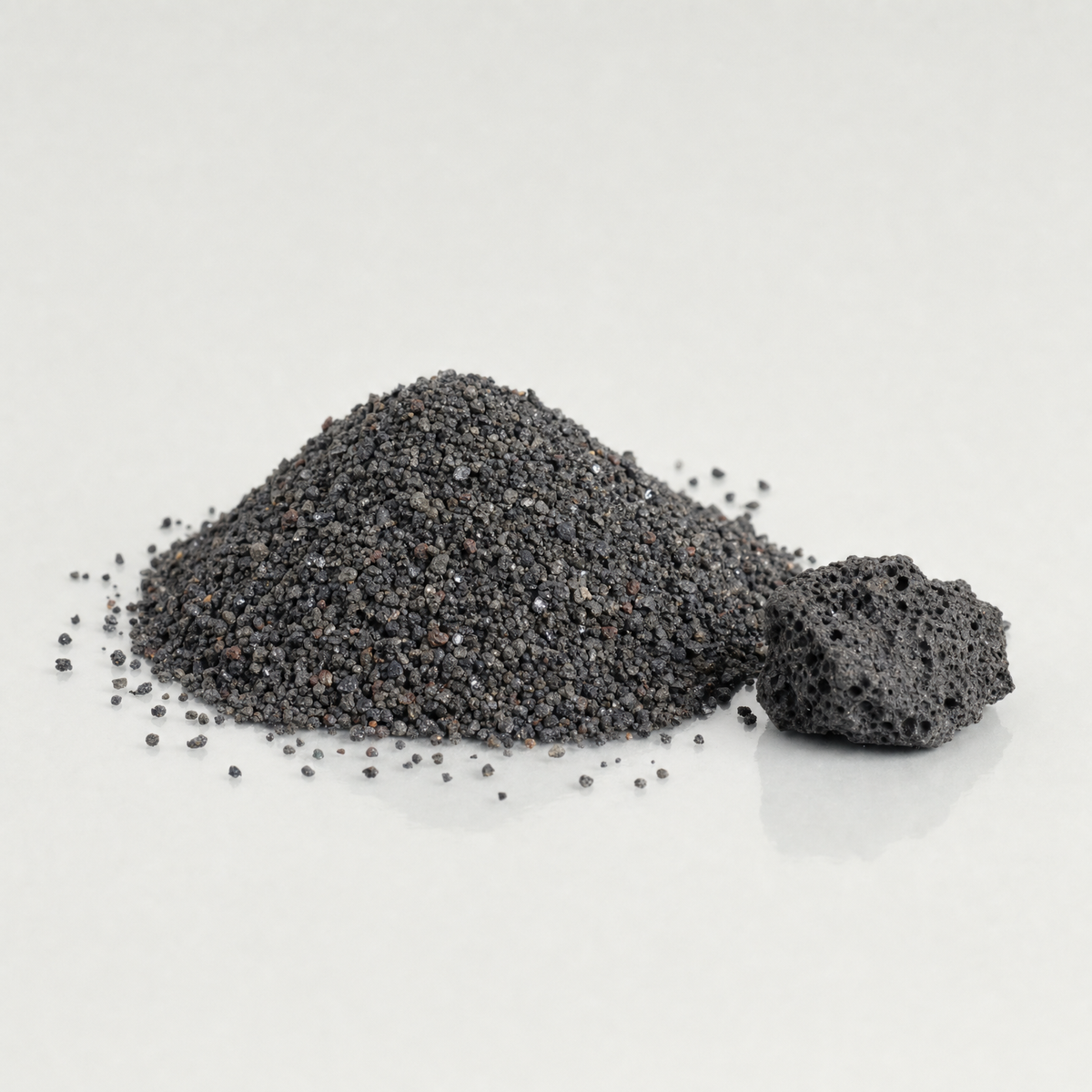 A heap of dark grey volcanic sand beside a piece of porous volcanic rock