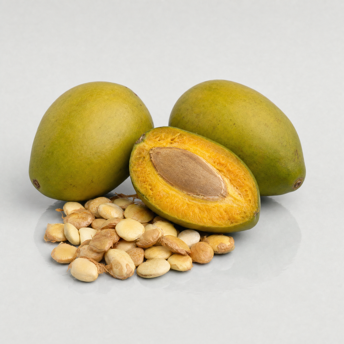 African wild mango fruits, one cut open to show its stone, beside a heap of pale dika nut kernels