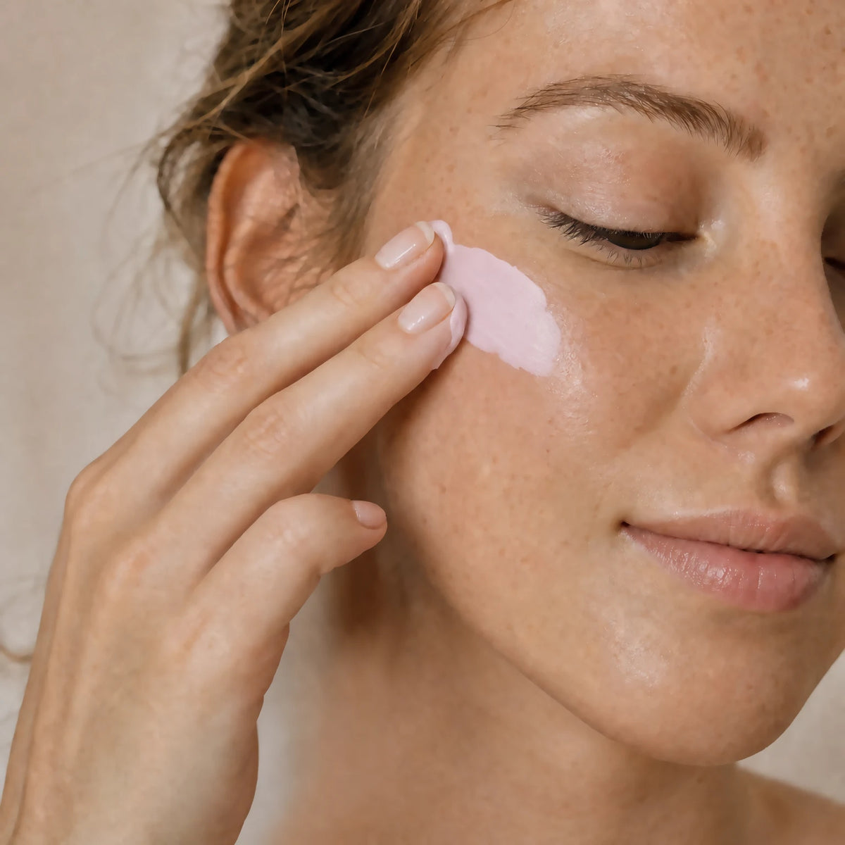 Woman with fair freckled skin smoothing pale pink Phyto-Exosome Radiance Serum onto her cheek with her fingertips