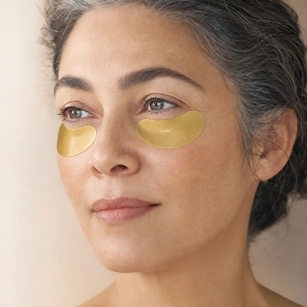 Woman wearing shimmering gold-toned Niacinamide Smoothing Eye Masks under both eyes